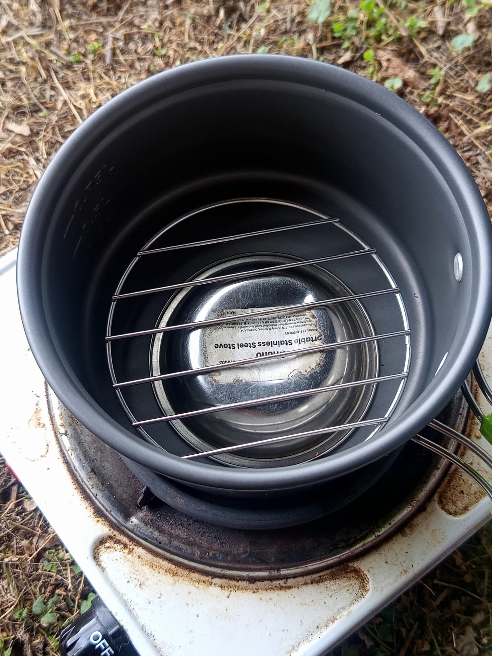 Improvisierter Campingbackofen: Campingtopf mit umgedrehter Metallschale und Metallgitter als Erhöhung